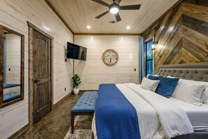 Une chambre à coucher avec un lit, un ventilateur de plafond, une télévision, une horloge murale et une fenêtre.