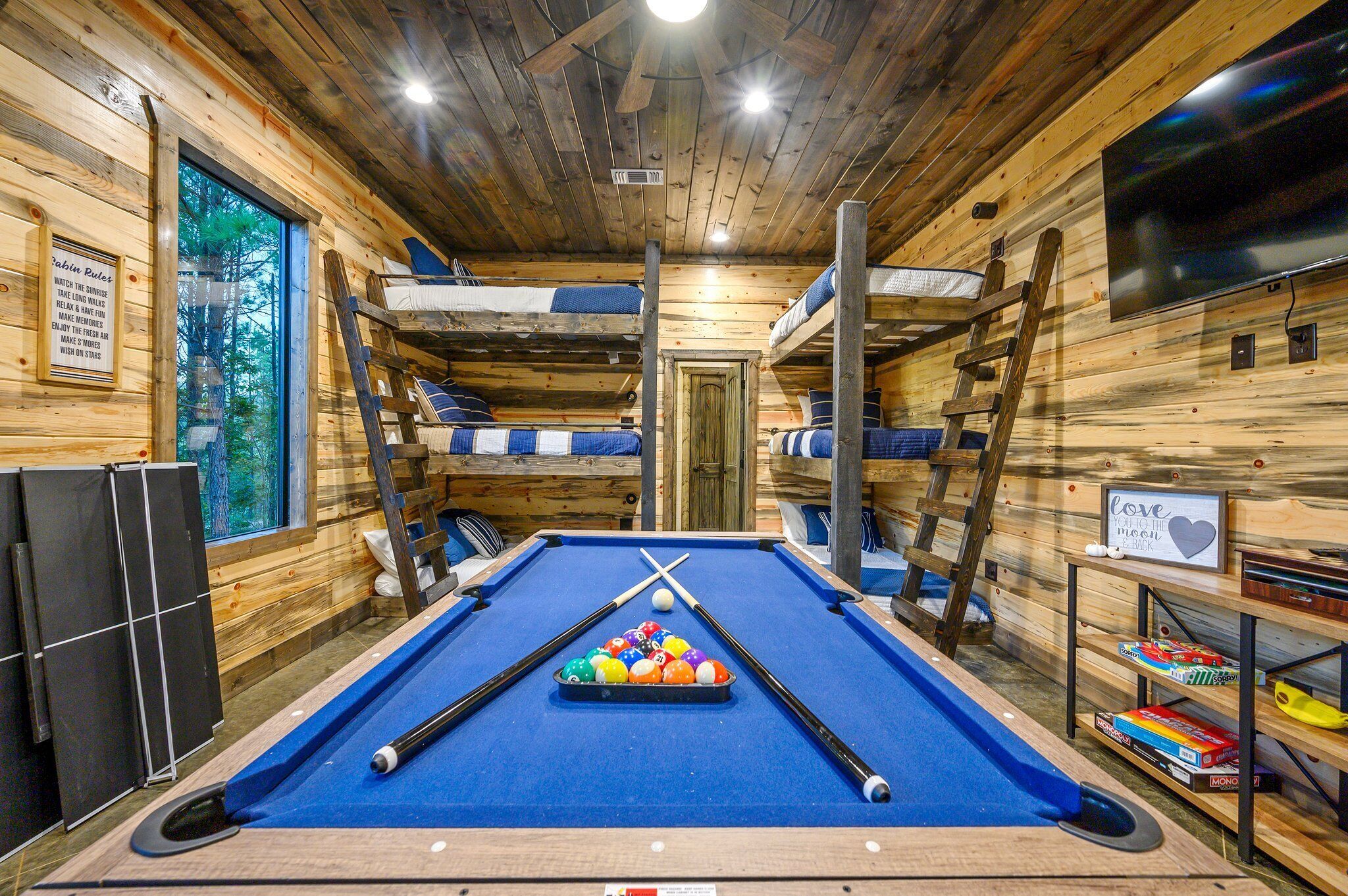 A pool table with billiard balls, bunk beds, a television, and a sign with a heart symbol.