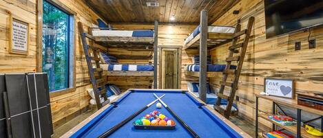 A pool table with billiard balls, bunk beds, a television, and a sign with a heart symbol.