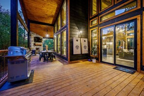 Une terrasse en bois avec un barbecue, un coin repas et de grandes fenêtres.