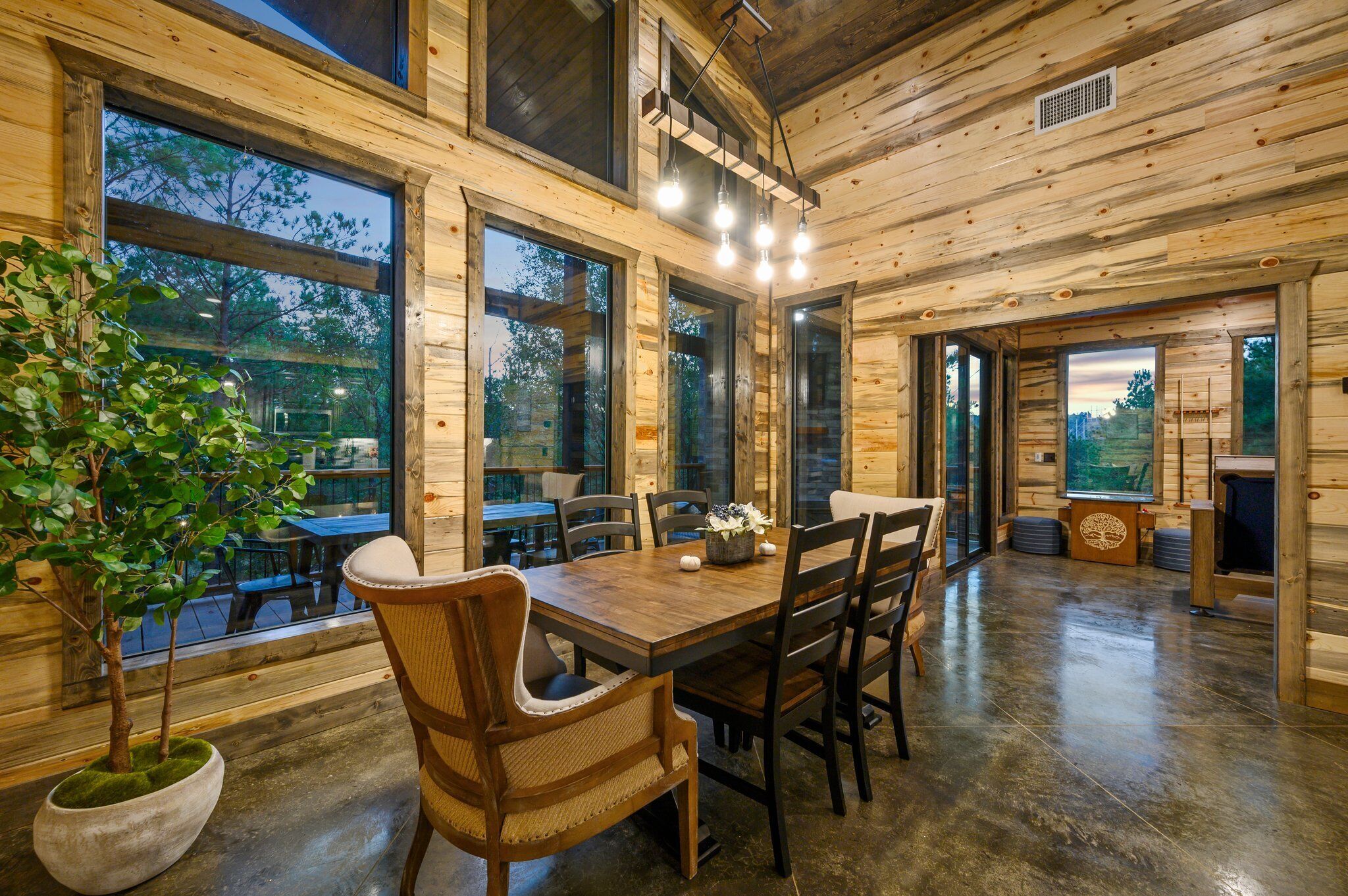 Un interior de madera con una mesa de comedor, sillas y ventanas grandes.