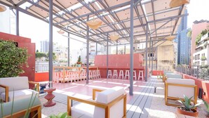 An outdoor seating area with tables and chairs, a red wall, and a view of the cityscape. - Dar Khawla (Beirut)
