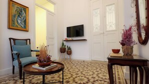 A living room with a television, a blue armchair, a coffee table with a book, and a patterned floor. - Dar Khawla (Beirut)