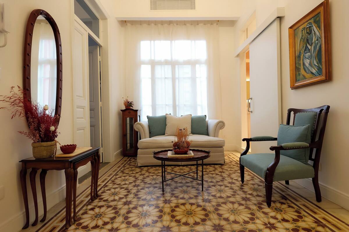 Un salón con suelo estampado, un sofá, un sillón, una mesa de centro, un espejo y un cuadro.
