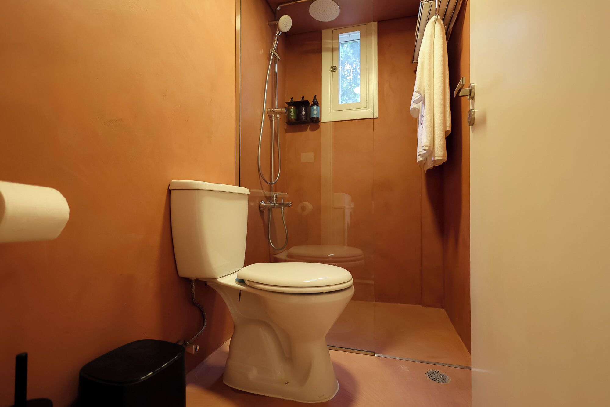 Un baño pequeño y funcional con inodoro, ducha y un ventanal.