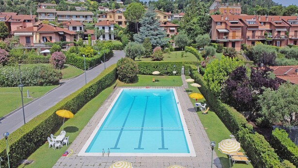 A swimming pool surrounded by neatly trimmed hedges and small trees, with a few chairs and umbrellas. - Villetta Bucaneve - Locz (Padenghe sul Garda)
