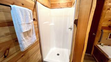 Une salle de bain rustique, avec des murs en bois, une douche, une serviette accrochée au mur et une porte en bois.