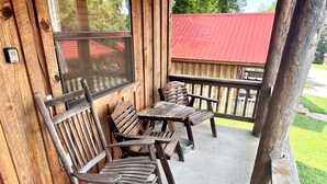A wooden porch with a table and chairs, a metal railing, and a view of a red-roofed building in the background. - Best Catch #49 Cabin in town, walking distance to the courthouse square. (Mountain View)