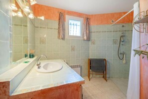 Casa de banho com lavatório, espelho, chuveiro e janela.