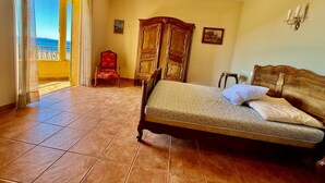A bedroom with a bed, a chair, a wardrobe, and a view of the sea through a door. - Maison en Bord de mer - Casa L'albitronu (Pietrosella)