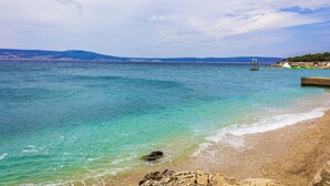 A coastal beach with clear turquoise waters, a rocky shoreline, and distant hills. - Studio with air conditioning, garden and terrace (Novi Vinodolski)