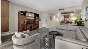 Una sala de estar con un sofá modular, un mueble para la televisión y un comedor con una mesa y sillas.