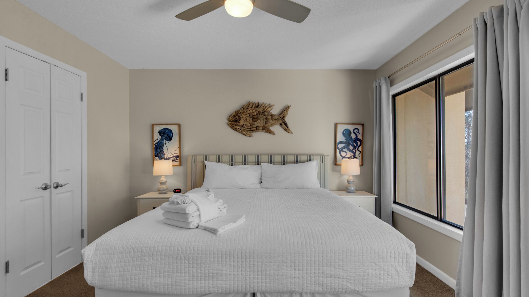 A hotel room with a large bed, two bedside lamps, a ceiling fan, and artwork on the walls.
