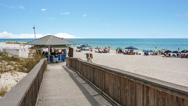 Una pasarela de madera que lleva a una playa con sombrillas y sillas.