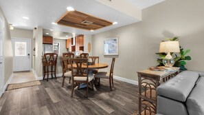 A dining area with a wooden table and chairs, a kitchen in the background, and a grey sofa with a lamp. - 1/2 Mile to the Beach at Sandestin + Pool: Lake Views at Beachwalk Villas (Miramar Beach)