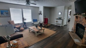 Ein Wohnzimmer mit Kamin, Deckenventilator und einem großen Fenster mit Jalousien.