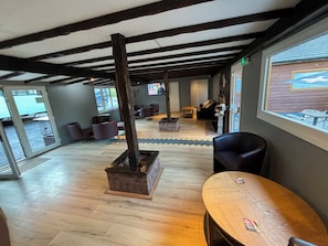A spacious indoor area with wooden flooring, a fireplace, seating arrangements, and large windows offering views outside.