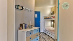 Un couloir étroit, avec un lit superposé sur le côté droit, une commode et une porte bleue.