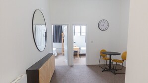 A room with a wooden cabinet, a round table with yellow chairs, a clock on the wall, and a door leading to another room.