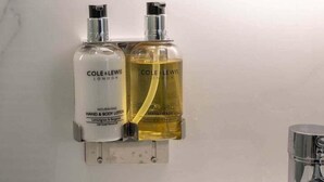 A bathroom with a white marble wall, a round mirror, and two bottles of Cole & Lewis hand and body lotion. - Cozy corner in London (London)