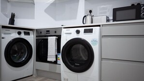 A laundry room with two Samsung washing machines, a kettle, and a microwave on a white countertop. - Cozy corner in London (London)