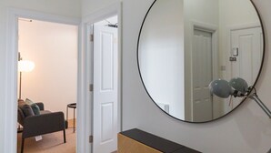 A room with a large round mirror on the wall, a door leading to another room, and a small table with a lamp. - Cozy corner in London (London)