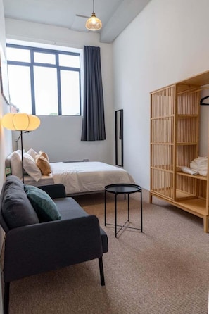 Ein modernes Schlafzimmer mit Bett, Sofa, einem kleinen Tisch, einem Kleiderschrank und einem Fenster mit Vorhängen.