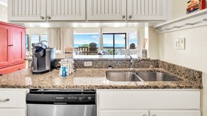 A kitchen with white cabinets, a granite countertop, a red cabinet, a coffee machine, and a view of the ocean. - ☀️Gulf Front Condo with Great Views-Latitude 29 #36☀️ (Panama City Beach)