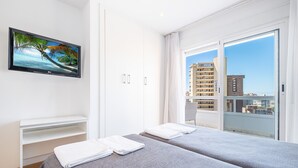 Habitación de hotel con balcón, televisor en la pared y cama con toallas.