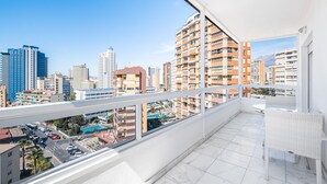 Un balcón con vista a la ciudad, muebles de mimbre blancos y suelo de baldosas.