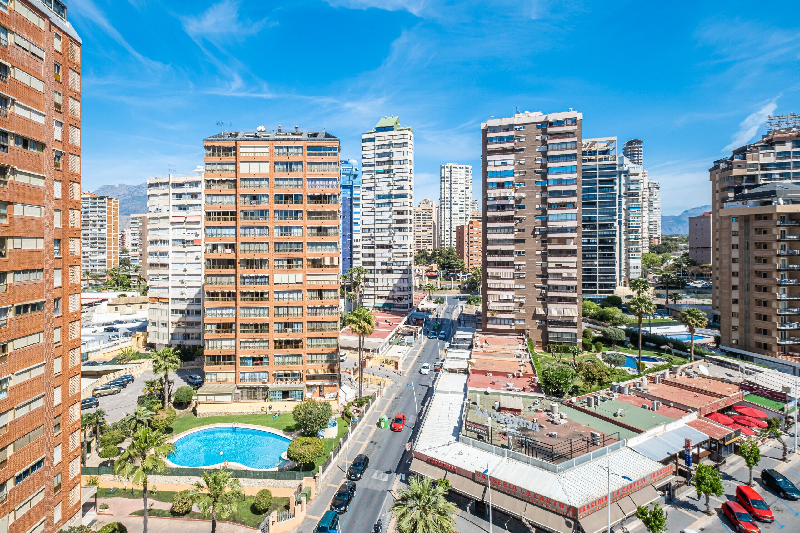 A high-rise building complex with multiple residential and commercial structures, a swimming pool, and a street with vehicles.