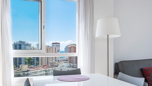 Una habitación moderna con vista a la ciudad, una mesa blanca, una lámpara y un sofá gris.