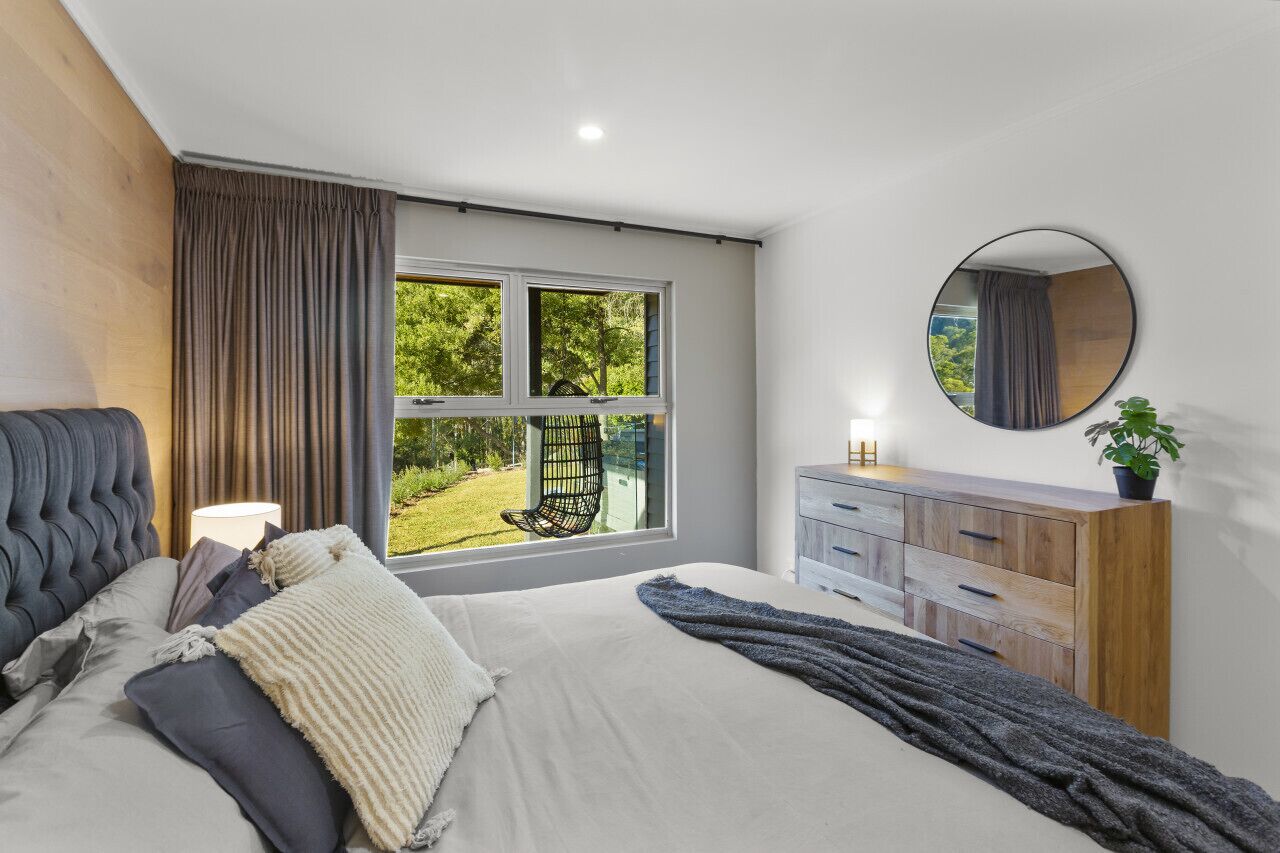 A bedroom with a large window, a bed, a dresser, and a mirror.