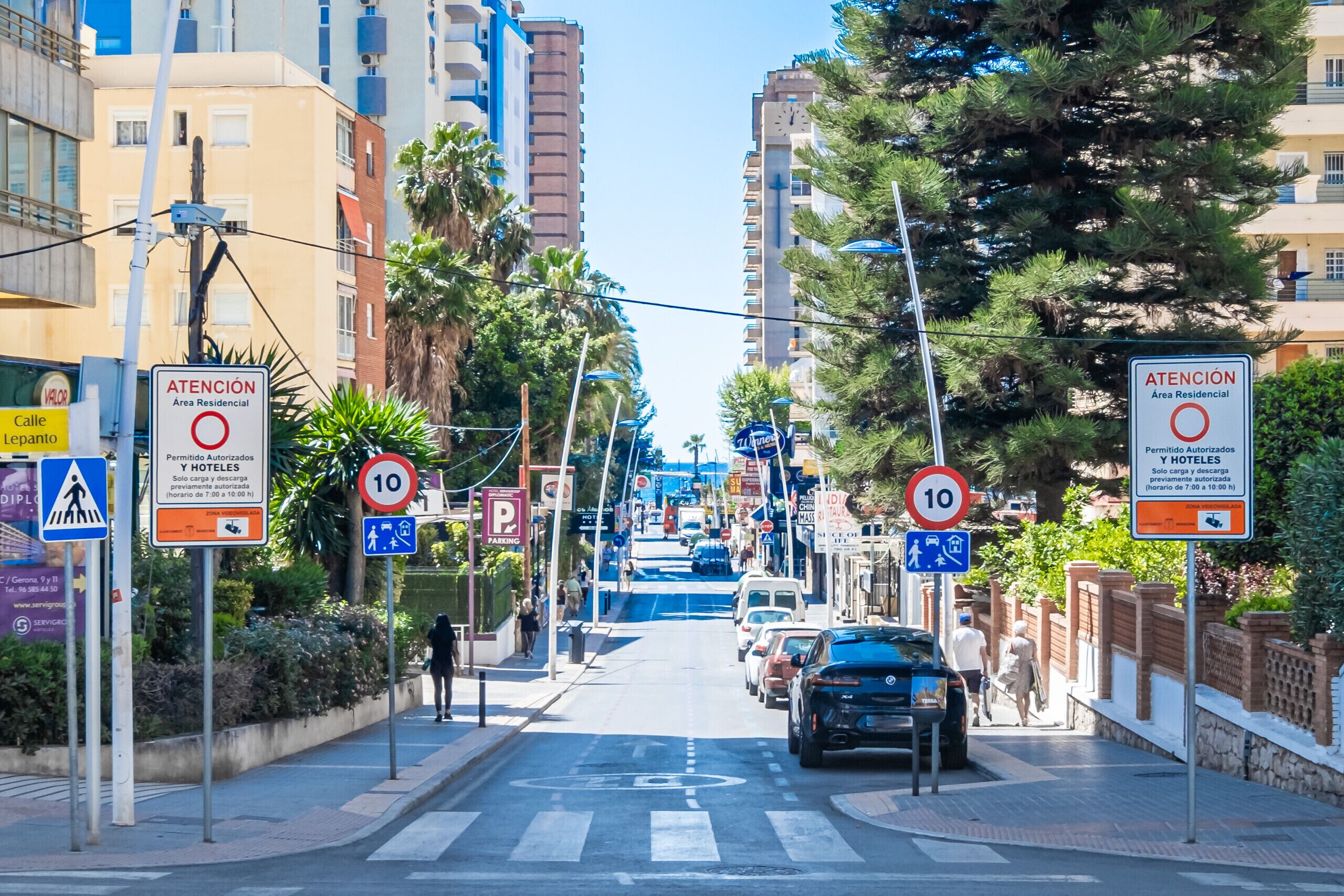 Una calle con varios carteles que indican restricciones de estacionamiento y un paso de peatones.