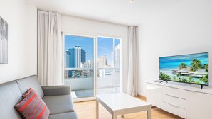Una sala de estar moderna con un sofá gris, una mesa de centro blanca y un televisor de pantalla plana sobre un mueble blanco.