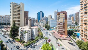 Un edificio de gran altura con varios pisos y balcones, rodeado de otros edificios altos y una calle concurrida llena de coches y peatones.