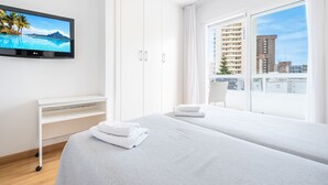 Una habitación de hotel moderna con una cama grande, un televisor en la pared, un escritorio y un balcón con vistas a la ciudad.