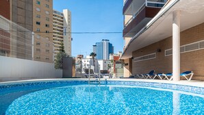 Una piscina con borde de azulejos, rodeada de edificios y un cielo despejado.