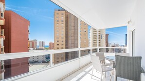 A balcony with a view of tall buildings, a table with chairs, and a railing.