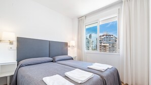 A hotel room with a large bed, two bedside tables, a window with curtains, and a view of city buildings.