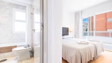 Une salle de bain moderne équipée de toilettes, d’un bidet et d’une douche. Une grande fenêtre offre une vue sur un bâtiment situé à l’extérieur.