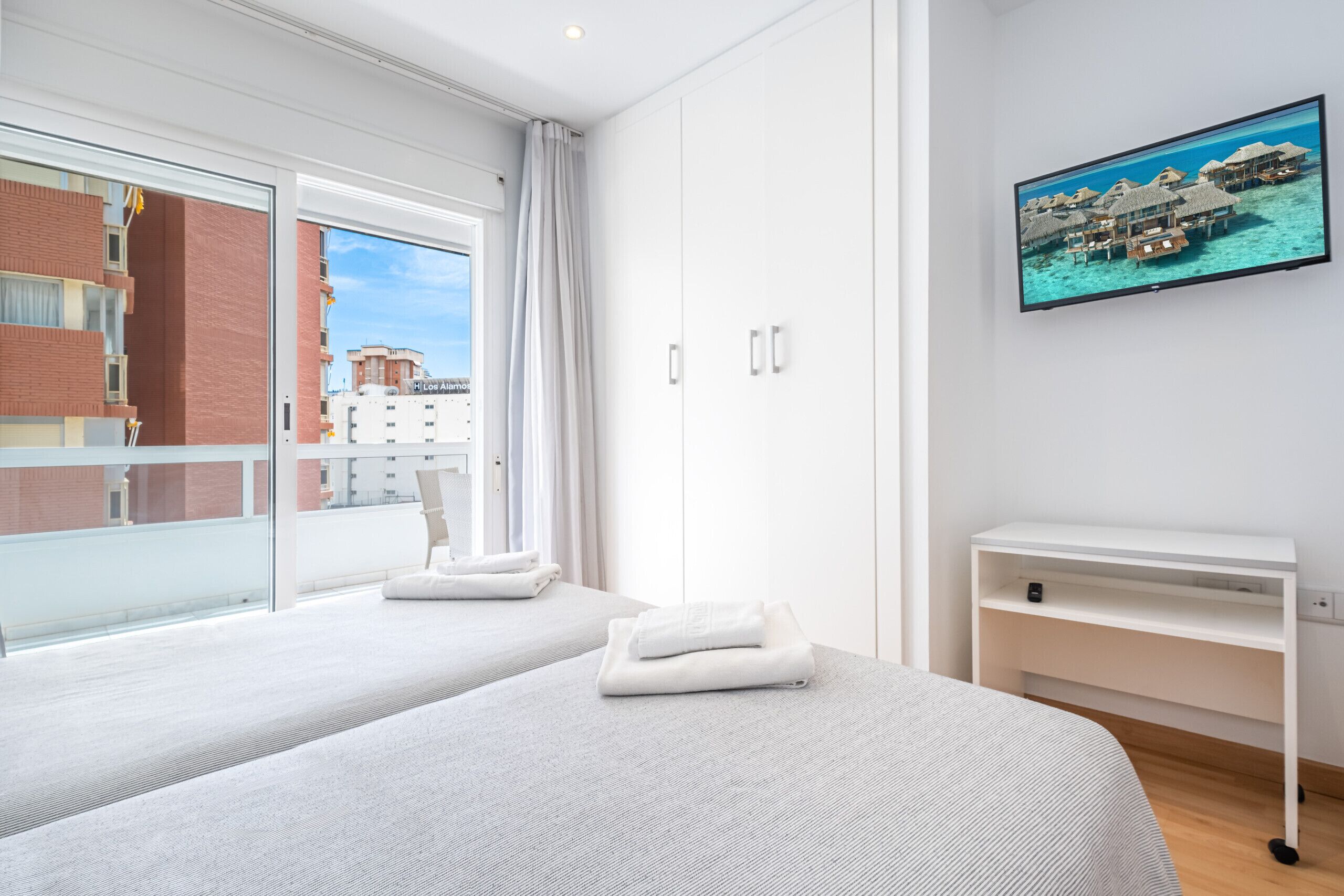 Een moderne hotelkamer met twee bedden, een televisie en een balkon met uitzicht op de stad.