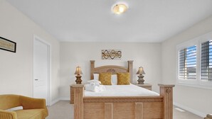 A bedroom with a wooden bed, two bedside tables, a chair, and a window with blinds. - Cozy home minutes from Niagara Falls (Thorold)