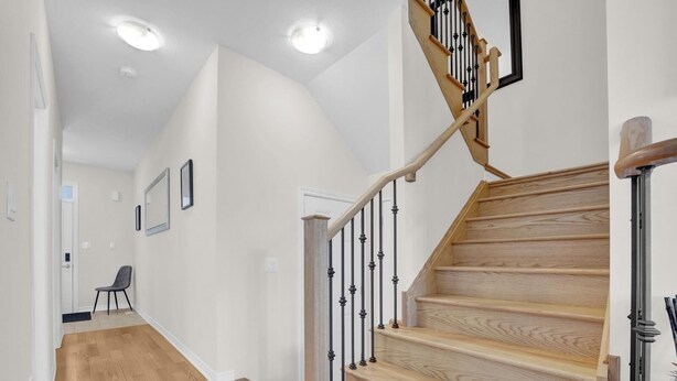 A staircase with wooden steps and black balusters, leading to a landing with a chair and framed pictures on the wall. - Cozy home minutes from Niagara Falls (Thorold)