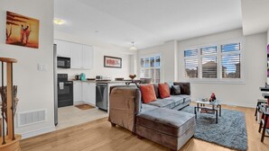 A modern living room with a grey sectional sofa, a wooden staircase, and a kitchen with white cabinets and a black refrigerator. - Cozy home minutes from Niagara Falls (Thorold)