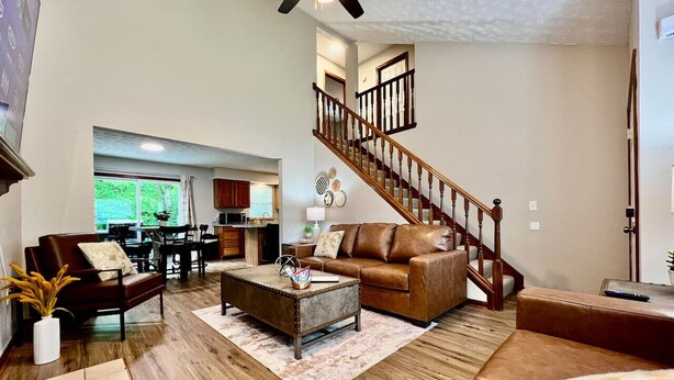 A spacious living room with a wooden staircase, a leather sofa, a coffee table, and a dining area in the background.