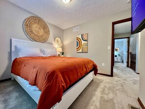 Une chambre à coucher comprenant un lit, une œuvre d’art accrochée au mur, une décoration murale en fibres tressées et un téléviseur.
