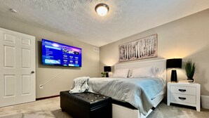 A bedroom with a bed, a TV mounted on the wall, a bedside table with a lamp, and a small plant.