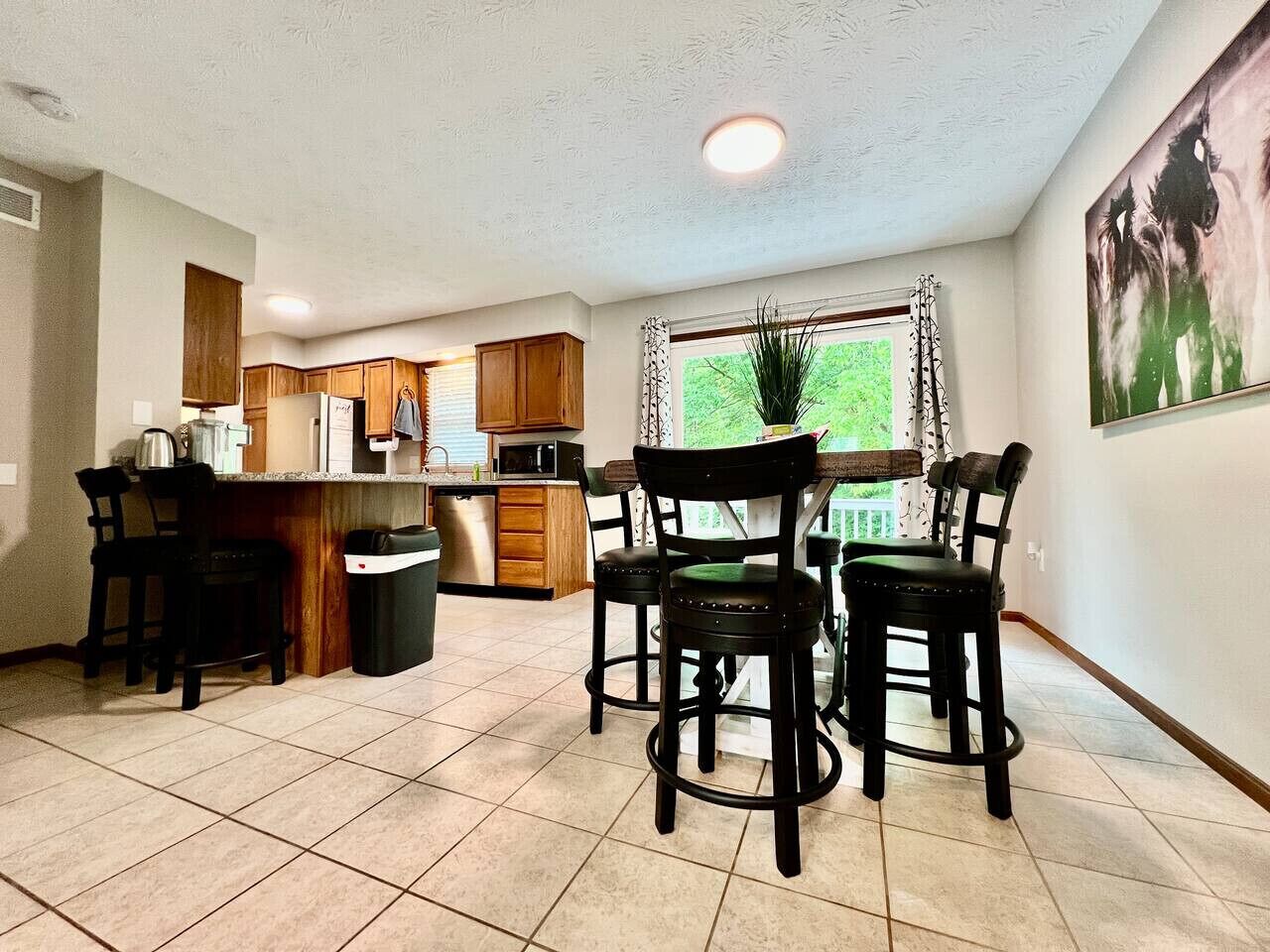 A kitchen with wooden cabinets, a dining area with four chairs, and a large window with curtains.