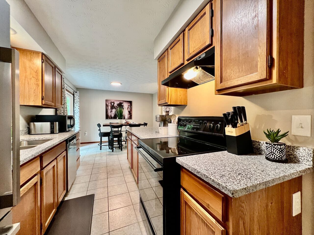A kitchen with wooden cabinets, a microwave, a stove, and a dining area with chairs and a table.